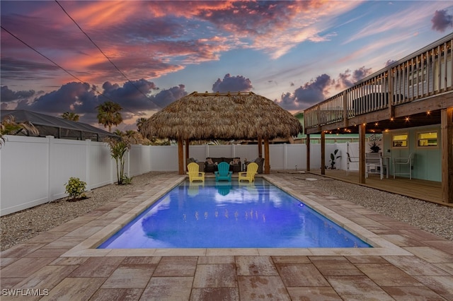 pool at dusk with a gazebo, a wooden deck, and a patio