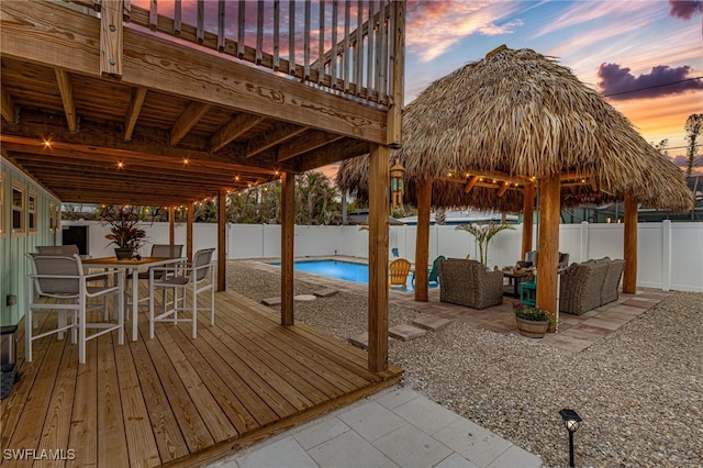 deck at dusk with an outdoor hangout area, a fenced in pool, and a patio area