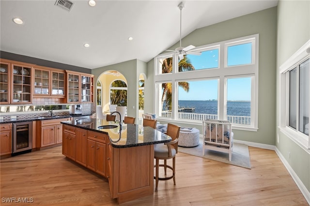 kitchen featuring sink, beverage cooler, dark stone counters, a kitchen island with sink, and a water view