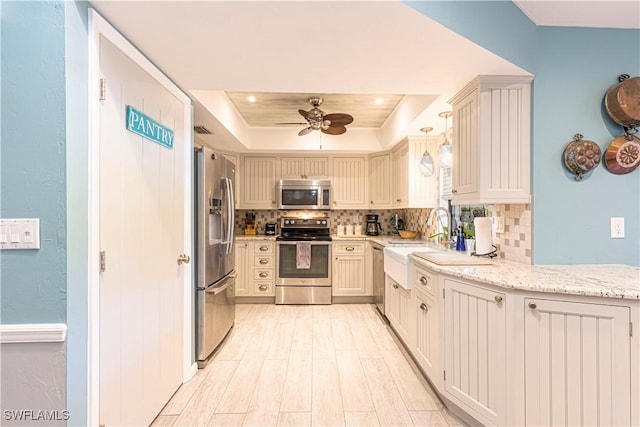 kitchen with a raised ceiling, hanging light fixtures, ceiling fan, appliances with stainless steel finishes, and tasteful backsplash