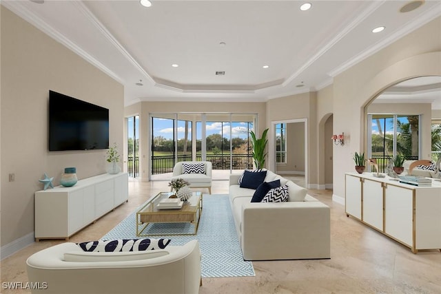 living room featuring a tray ceiling, plenty of natural light, arched walkways, and ornamental molding