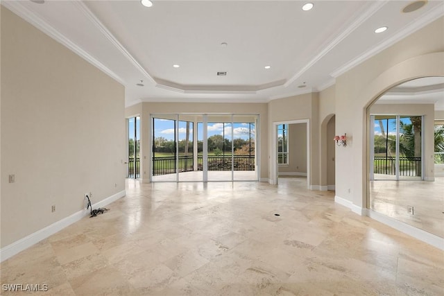 empty room featuring a tray ceiling, plenty of natural light, baseboards, and arched walkways