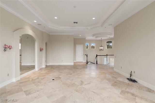 unfurnished room with a tray ceiling, arched walkways, baseboards, and crown molding