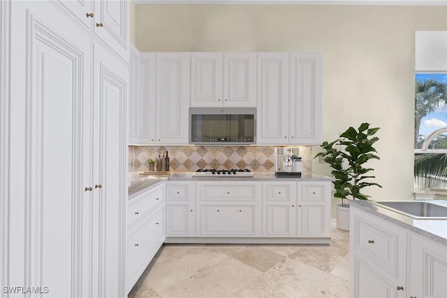 kitchen featuring stainless steel microwave, white cabinets, white gas stovetop, tasteful backsplash, and a sink