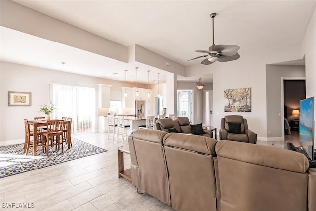 living area with a ceiling fan, plenty of natural light, and baseboards