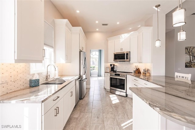 kitchen with light stone counters, a sink, white cabinetry, hanging light fixtures, and appliances with stainless steel finishes