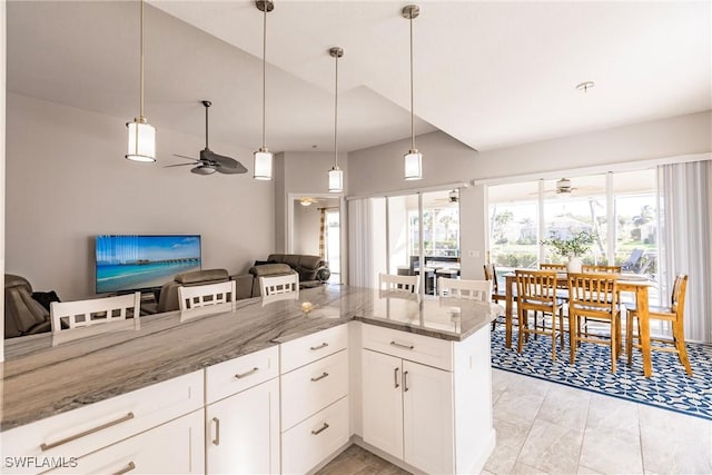 kitchen featuring hanging light fixtures, stone countertops, white cabinetry, and open floor plan