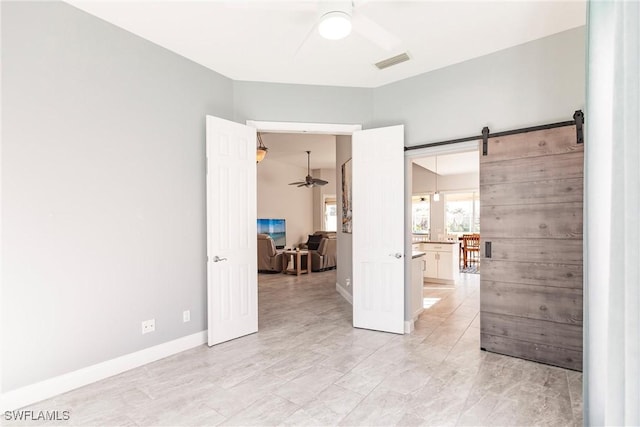 empty room with baseboards, a barn door, visible vents, and a ceiling fan