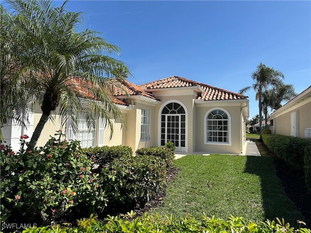 rear view of property featuring a yard, a tile roof, and stucco siding