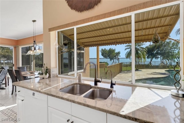 kitchen featuring a water view, light stone counters, white cabinets, decorative light fixtures, and sink