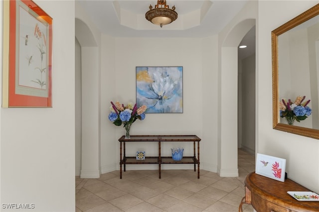 hall featuring light tile patterned flooring and a raised ceiling