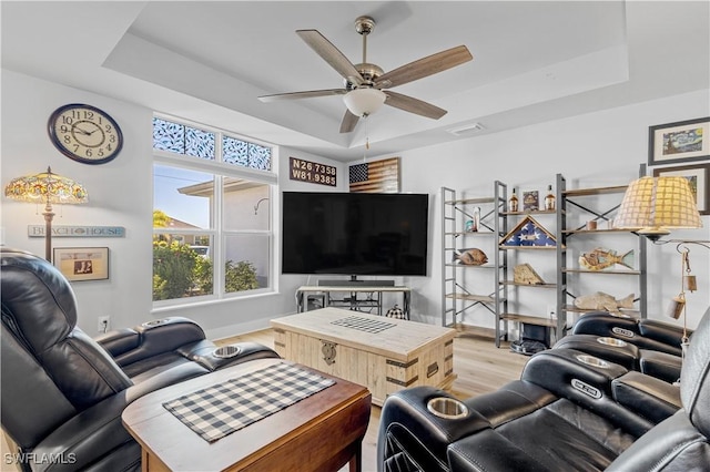 living room featuring ceiling fan, a raised ceiling, and light hardwood / wood-style flooring