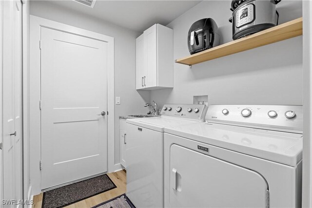 clothes washing area featuring cabinets, washer and clothes dryer, light hardwood / wood-style floors, and sink