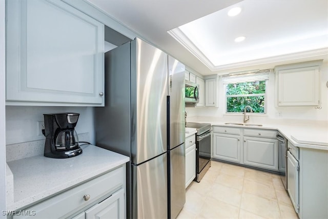 kitchen featuring appliances with stainless steel finishes, ornamental molding, a raised ceiling, sink, and gray cabinets