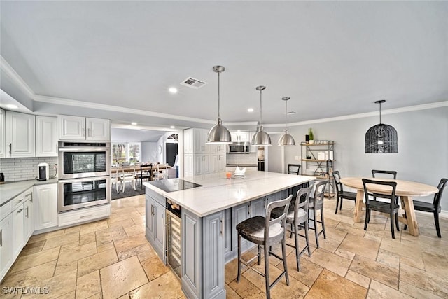 kitchen featuring white cabinets, a spacious island, hanging light fixtures, appliances with stainless steel finishes, and light stone counters