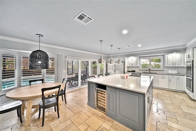 kitchen with pendant lighting, backsplash, crown molding, wine cooler, and a kitchen island