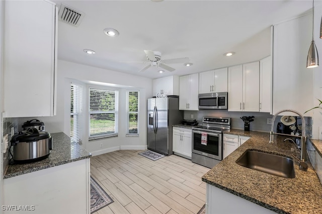 kitchen featuring stainless steel appliances, sink, light hardwood / wood-style flooring, dark stone countertops, and white cabinetry