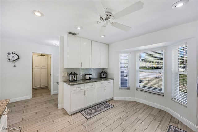 kitchen with backsplash, dark stone countertops, white cabinets, and light wood-type flooring