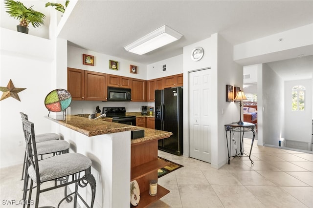 kitchen with a breakfast bar, black appliances, dark stone countertops, light tile patterned floors, and kitchen peninsula