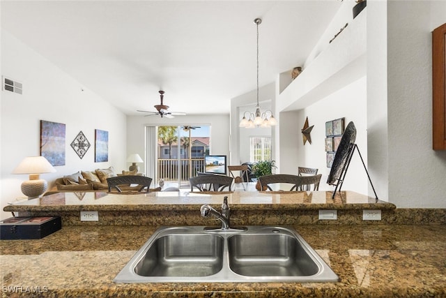 kitchen with decorative light fixtures, sink, ceiling fan with notable chandelier, and dark stone counters