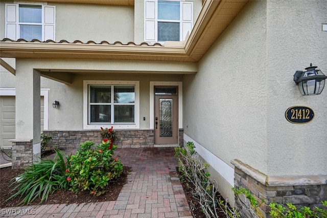 view of exterior entry featuring stone siding and stucco siding