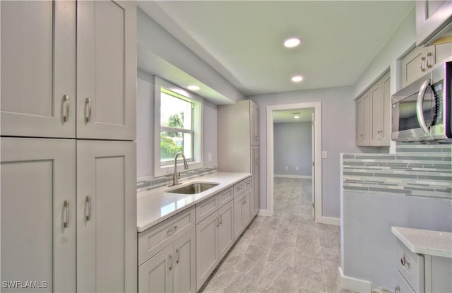 kitchen featuring tasteful backsplash, gray cabinets, light stone counters, and sink