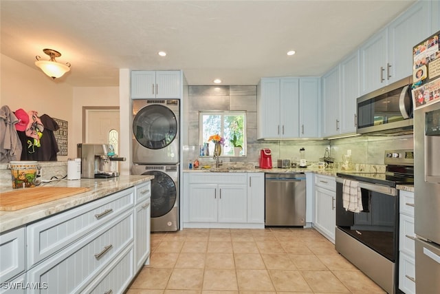 kitchen featuring white cabinetry, tasteful backsplash, stacked washer / dryer, stainless steel appliances, and light stone countertops