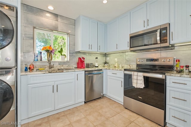 kitchen featuring light tile patterned floors, stacked washing maching and dryer, stainless steel appliances, white cabinets, and decorative backsplash