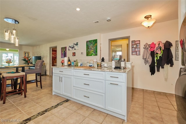 kitchen with light tile patterned flooring, stacked washer and clothes dryer, decorative light fixtures, light stone countertops, and white cabinets