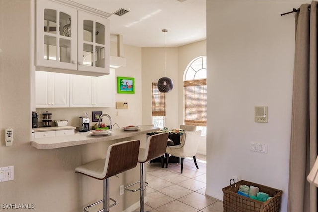 kitchen featuring kitchen peninsula, light tile patterned floors, decorative light fixtures, a kitchen bar, and white cabinetry