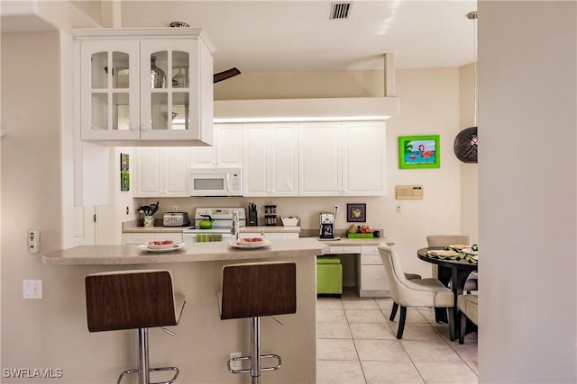 kitchen with white cabinetry, vaulted ceiling, white appliances, a kitchen bar, and light tile patterned floors