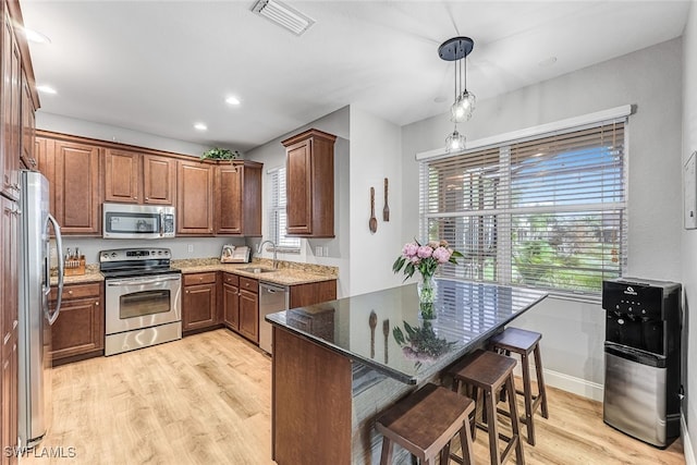 kitchen with stainless steel appliances, a kitchen breakfast bar, dark stone counters, decorative light fixtures, and light wood-type flooring