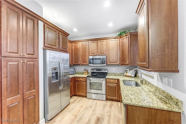 kitchen featuring sink, light stone countertops, stainless steel appliances, and light hardwood / wood-style flooring