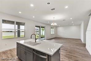 kitchen featuring stainless steel dishwasher, sink, light hardwood / wood-style flooring, a notable chandelier, and an island with sink