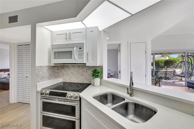 kitchen with white cabinetry, range with two ovens, decorative backsplash, and sink