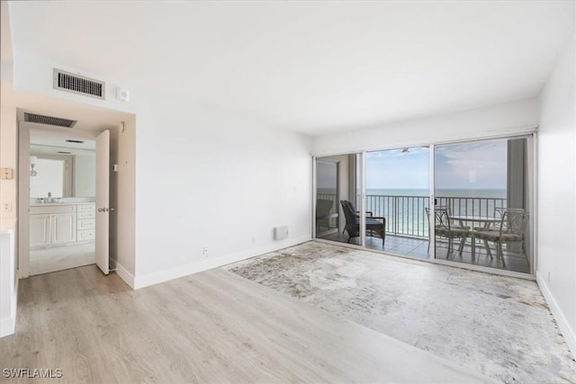 unfurnished room with light wood-type flooring, a water view, and sink