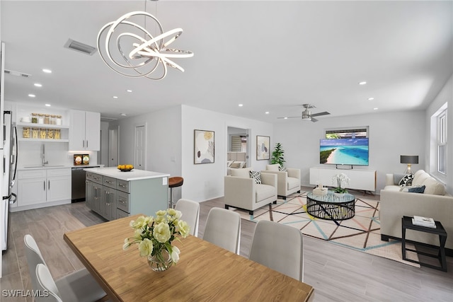 dining space featuring ceiling fan with notable chandelier, light hardwood / wood-style floors, and sink