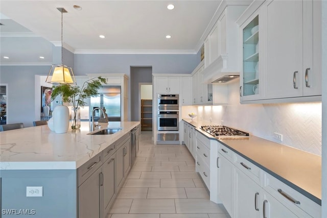 kitchen with a large island with sink, sink, appliances with stainless steel finishes, decorative light fixtures, and white cabinetry