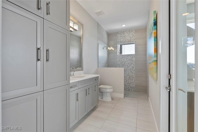 bathroom featuring toilet, tile patterned flooring, vanity, and tiled shower