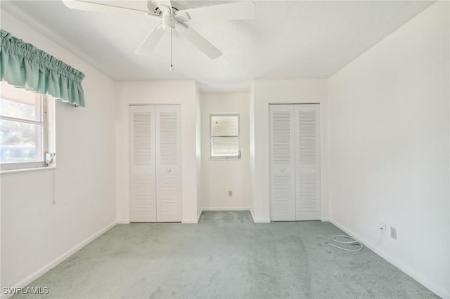 unfurnished bedroom with multiple closets, ceiling fan, and light colored carpet