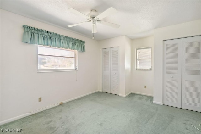 unfurnished bedroom featuring multiple closets, light carpet, ceiling fan, and a textured ceiling