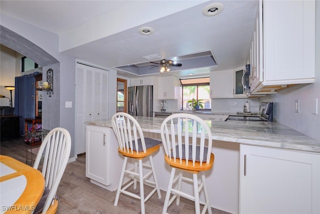 kitchen featuring a breakfast bar, ceiling fan, appliances with stainless steel finishes, light hardwood / wood-style floors, and white cabinetry