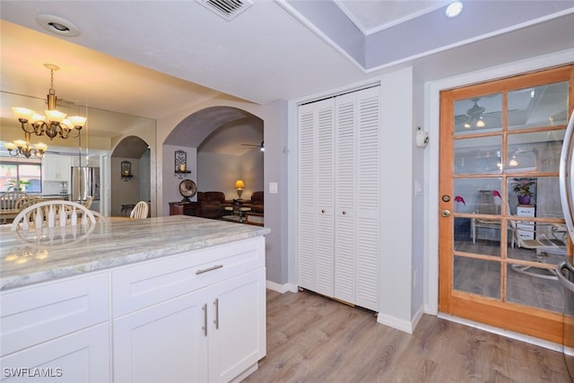 kitchen featuring stainless steel fridge, light stone counters, light hardwood / wood-style flooring, white cabinets, and hanging light fixtures