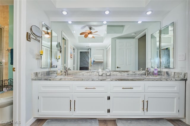 bathroom with vanity, ceiling fan, a tray ceiling, an enclosed shower, and wood-type flooring