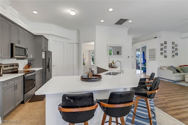 kitchen with a breakfast bar, sink, light hardwood / wood-style flooring, gray cabinets, and stainless steel appliances