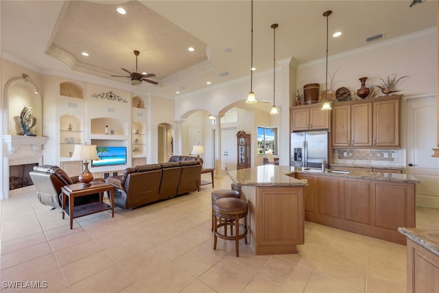 kitchen with stainless steel fridge, decorative light fixtures, a kitchen island with sink, and a tray ceiling