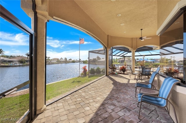 view of patio featuring a lanai, ceiling fan, and a water view