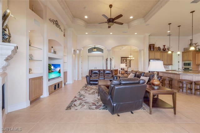 tiled living room with ceiling fan with notable chandelier, built in features, ornamental molding, and ornate columns