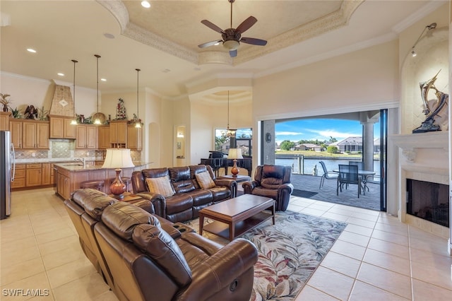 tiled living room with a raised ceiling, ceiling fan, and ornamental molding