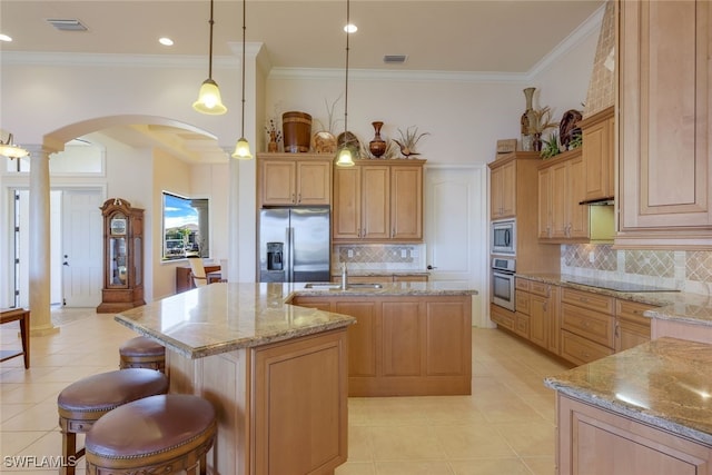 kitchen featuring hanging light fixtures, light stone counters, decorative columns, a center island with sink, and appliances with stainless steel finishes